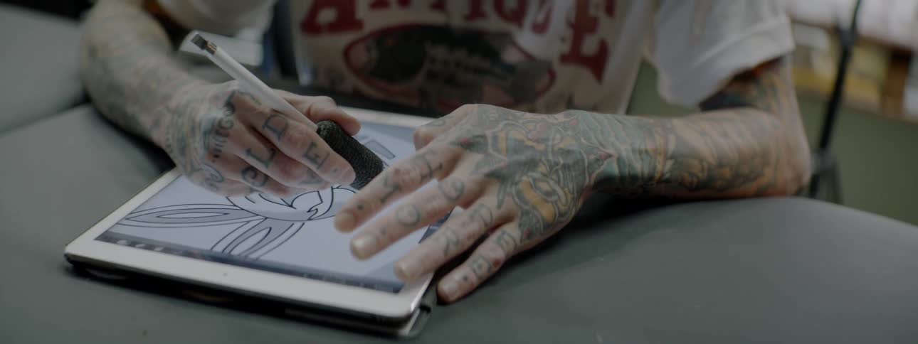 A tattoo artist designs a tattoo on a tablet in a studio