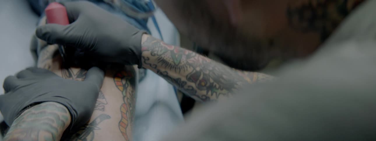 A male tattoo artist tattooing an arm
