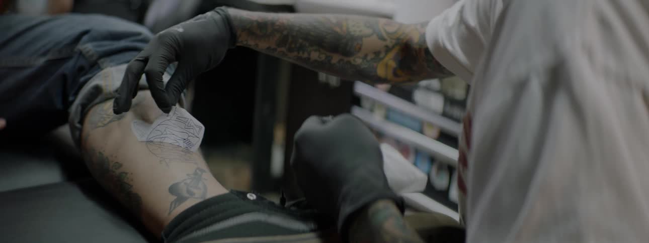 Tattoo artist applies stencil to man's leg