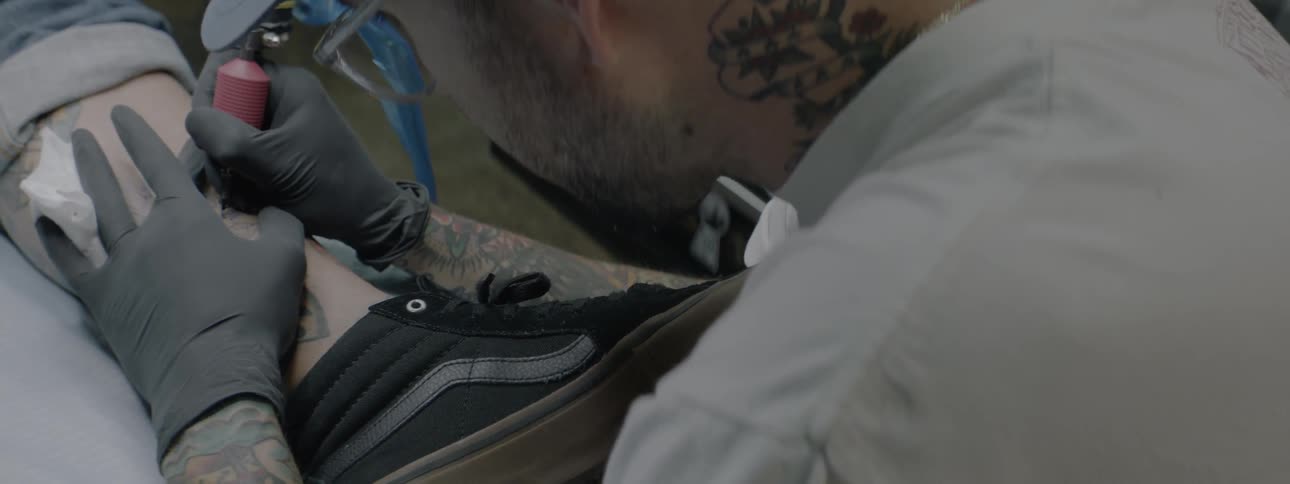 A male tattoo artist is inking a design on a customers leg
