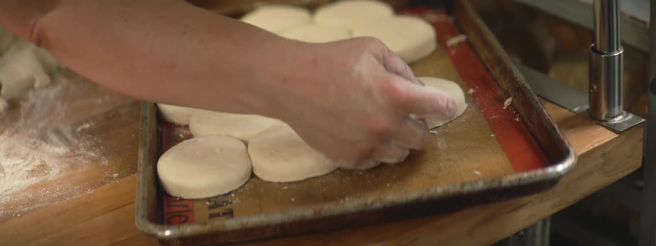 Man kneads dough and puts them on the tray indoors during the daytime