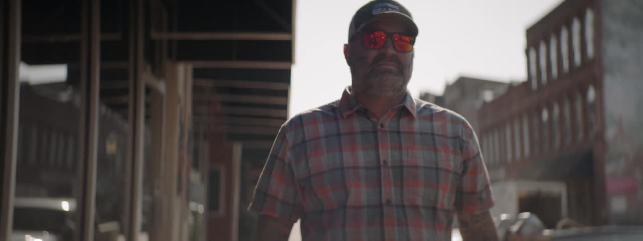 Middle aged man wearing cap and sunglasses walks down the street in the city on a sunny day