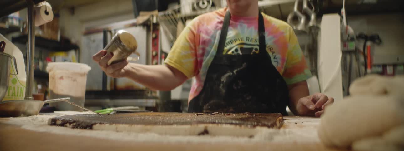 A woman is shaking powder of a table full of pastries