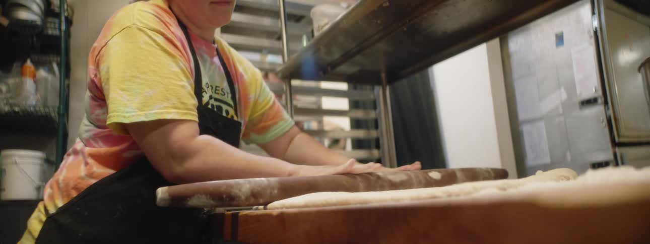 A white woman in an apron kneads dough with a rolling pin