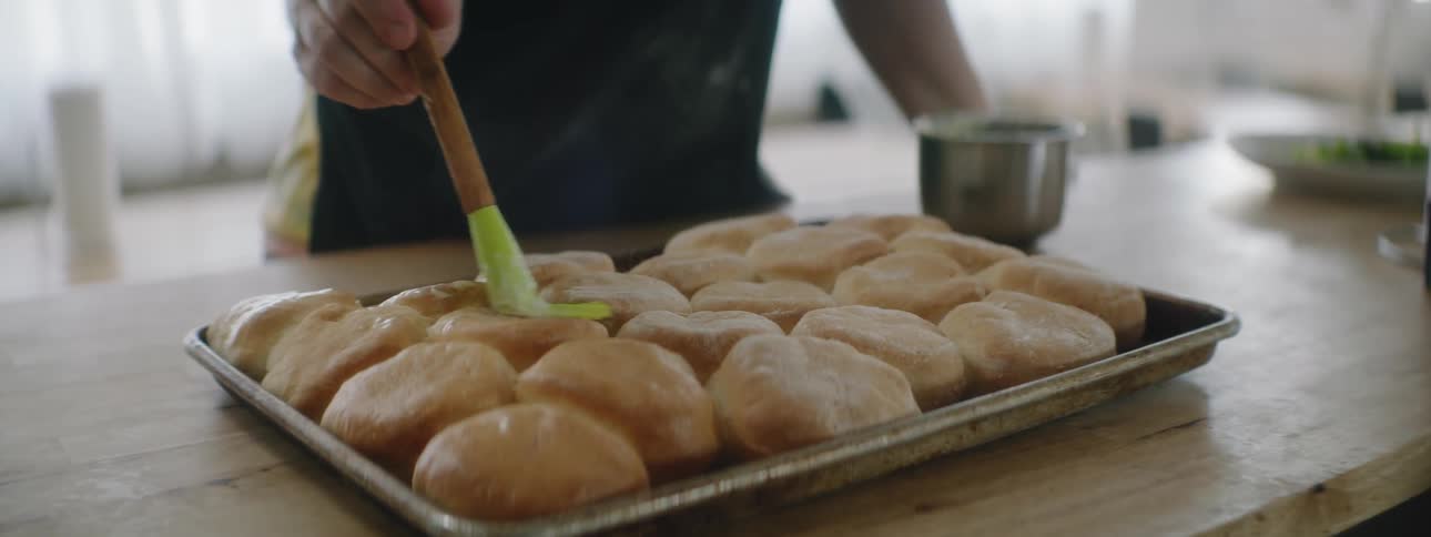 A chef is putting glaze on buns in the kitchen