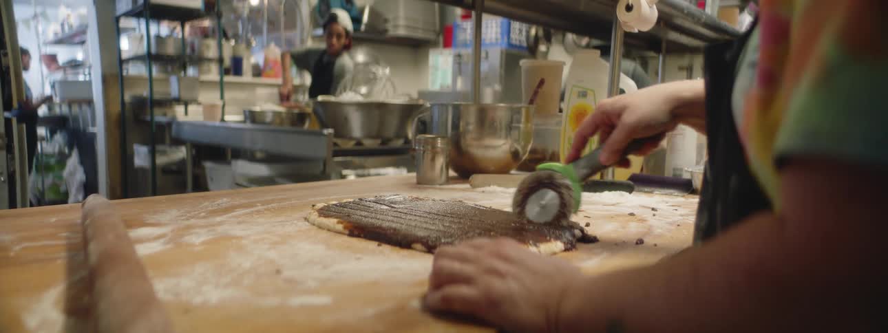 Food service worker seasons and slices bread in commercial kitchen