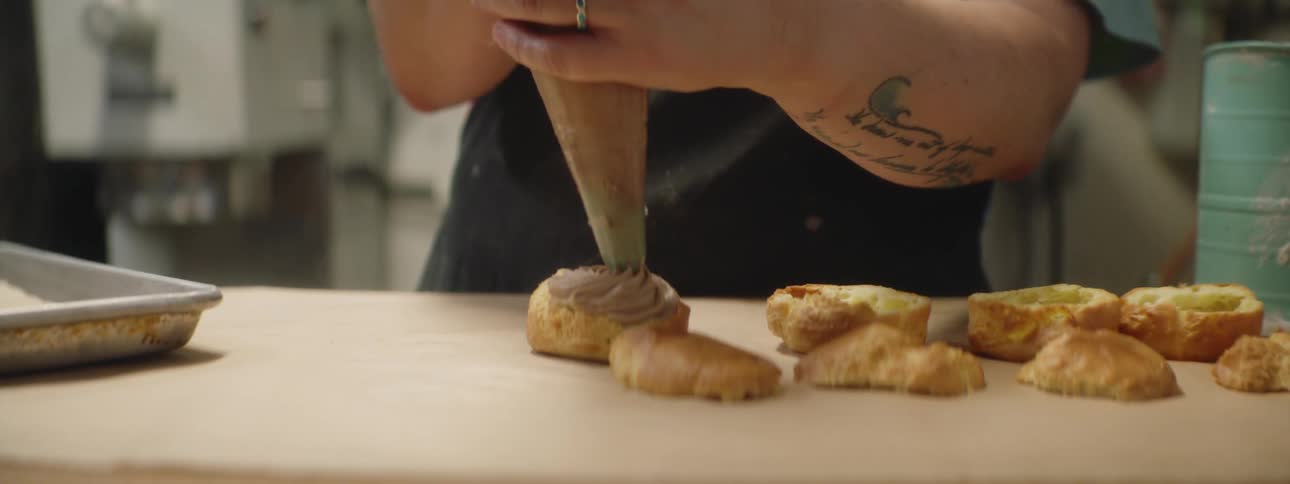 A baker pipes cream into a pastry puff