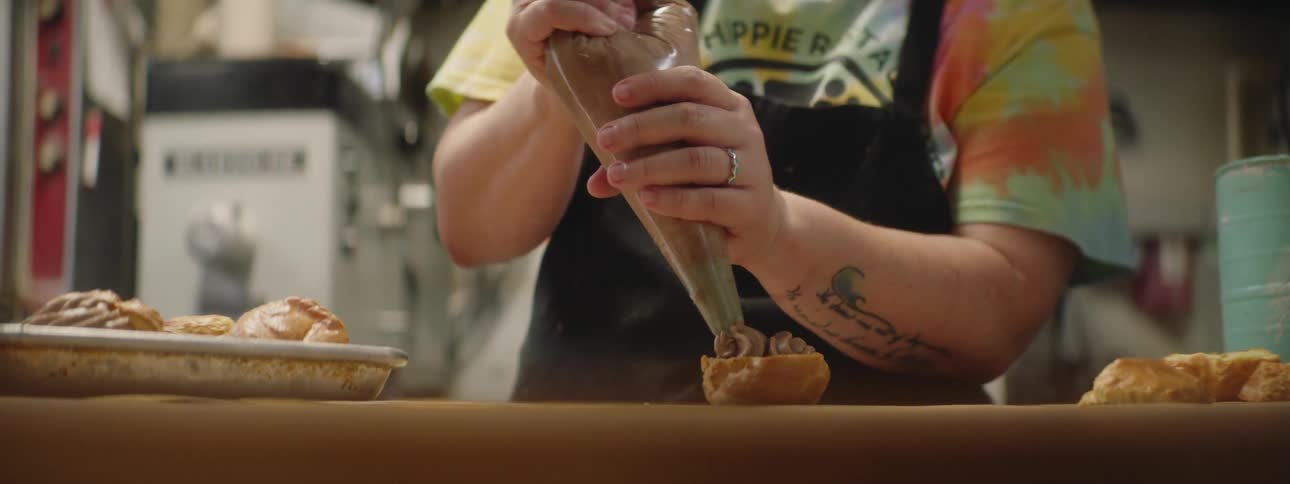 A bake squeezing fudge icing onto a pastry