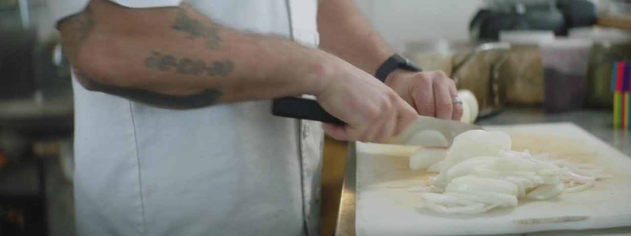 Cook peels onion with knife on the cut board in the kitchen