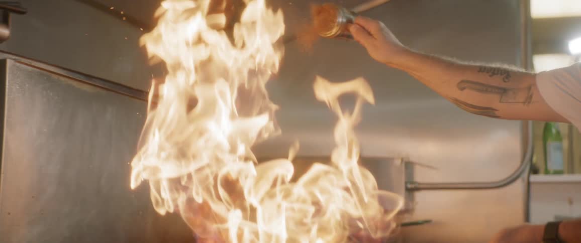 A chef putting seasoning on a pan that is on fire