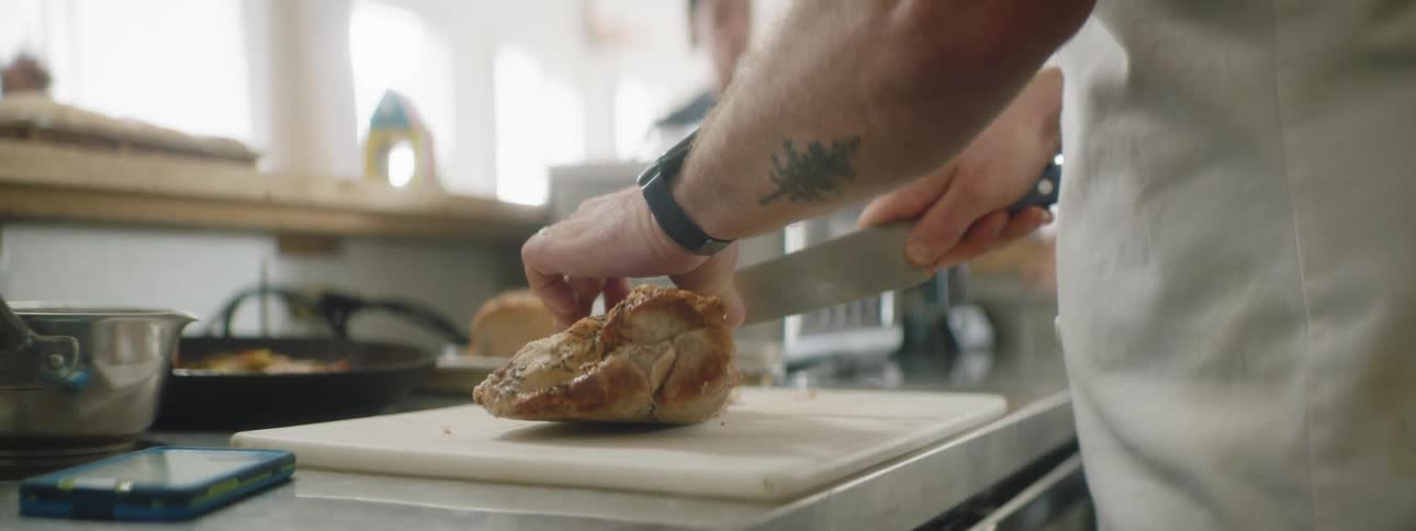 A man slices a cooked chicken with a knife on a cutting board