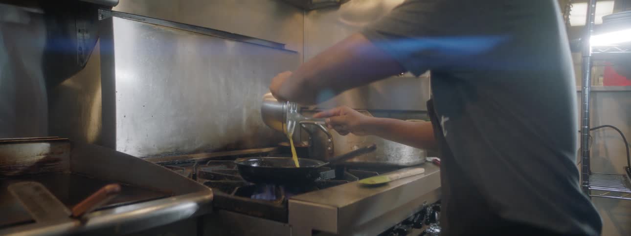 A cook pours liquid eggs into a frying pan