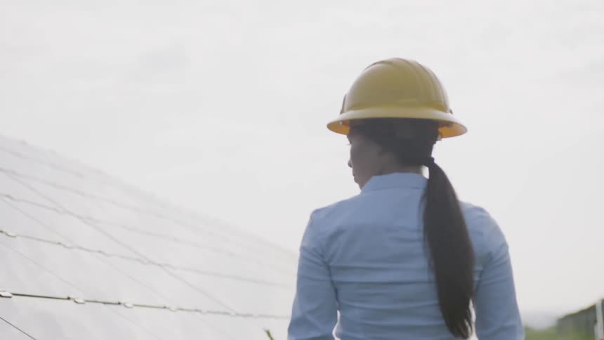 Woman wearing a hard hat walks around a solar panel array