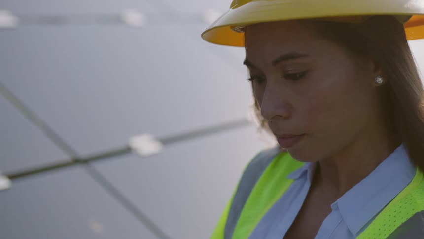 A female worker in a hard hat and safety vest using a laptop
