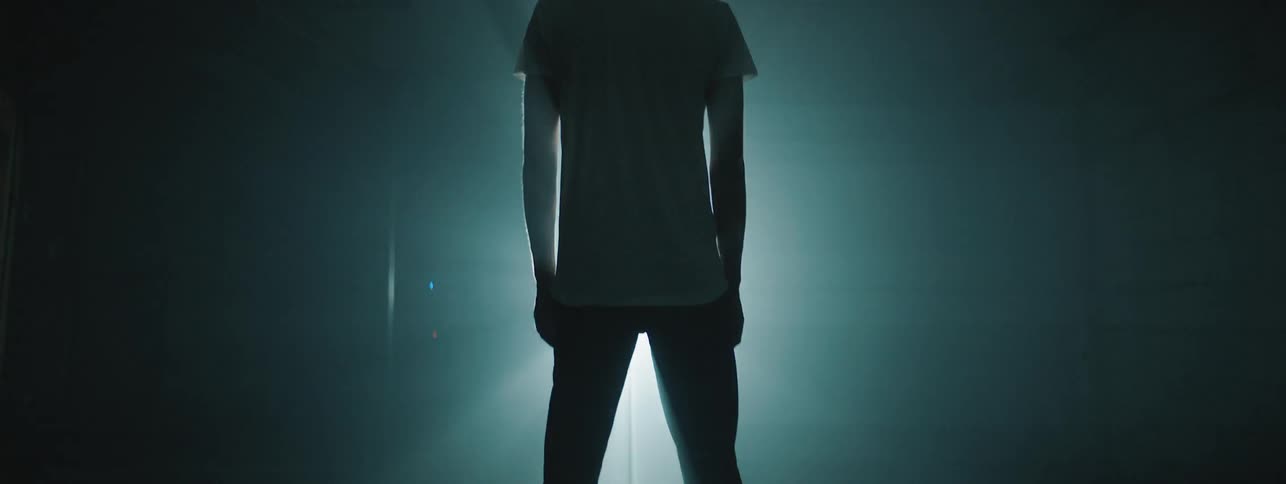 Man standing on a dim lit room in front of a light source