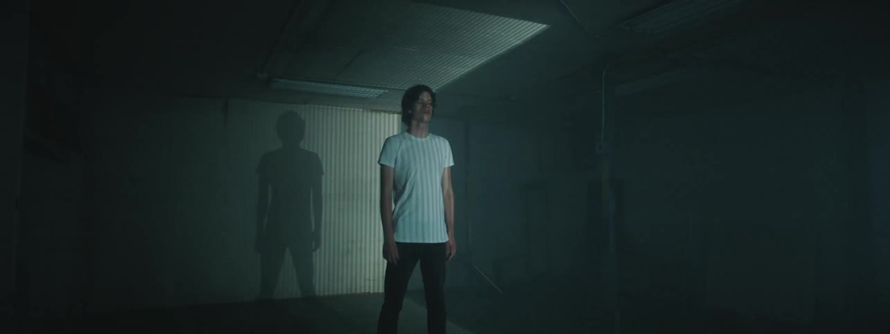 A man stands with his eyes closed in a container while a strobe light flashes across the room
