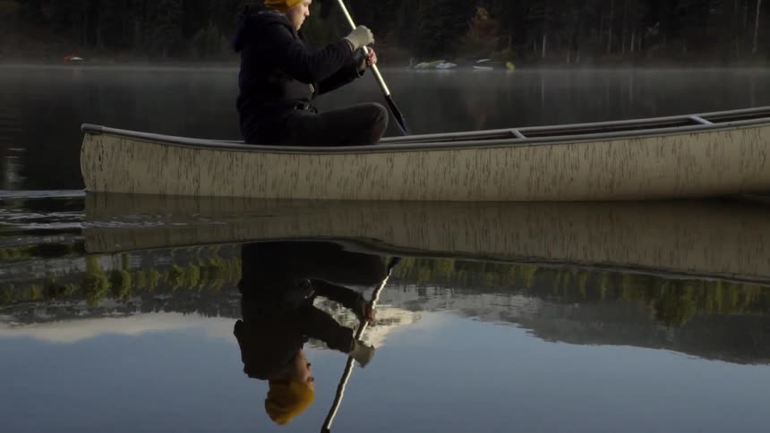 A man is rowing down a river with a forest in the background