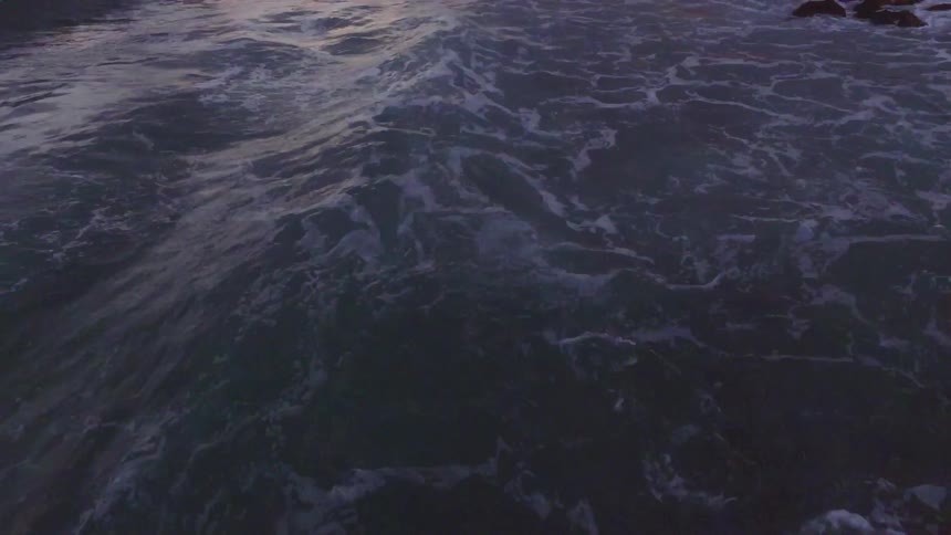 Water flows and foams along the shoreline at dusk