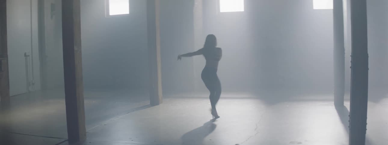 A woman dances in high heels in a hazy room