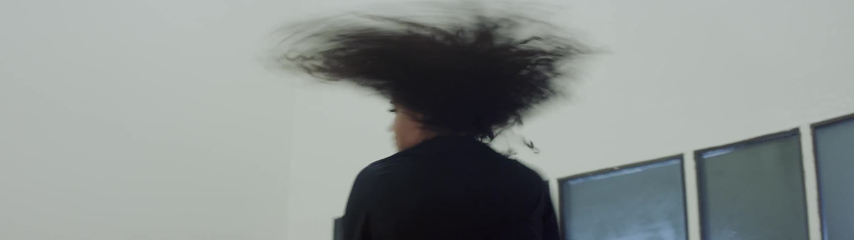 A young woman with long curly black hair dances very intensely as she moves her arms in an excited manner while jumping and spinning