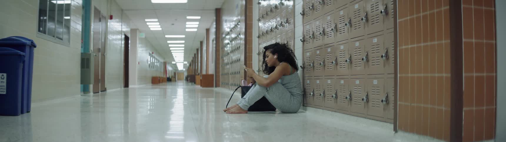 A young girl sits in an empty school hallway