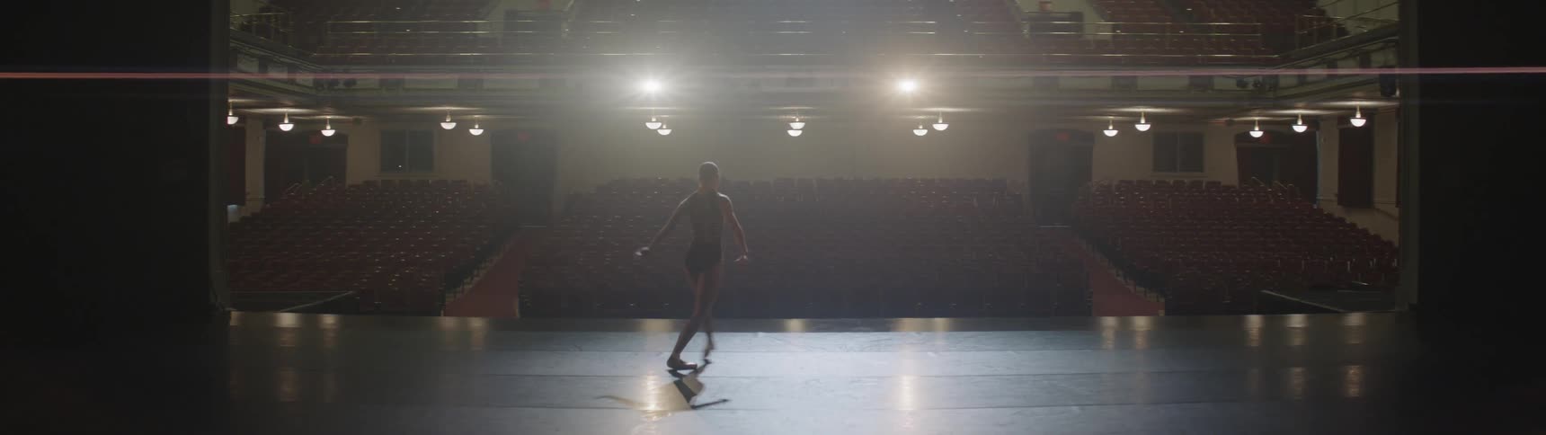 A ballerina performs on stage in an empty theater