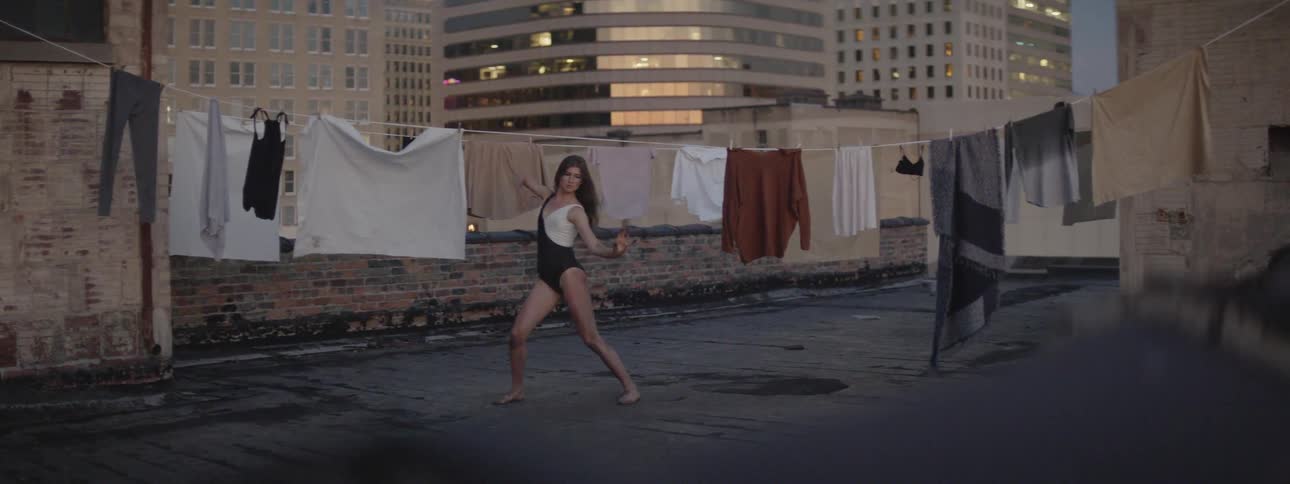 A woman dances on a roof next to a clothesline