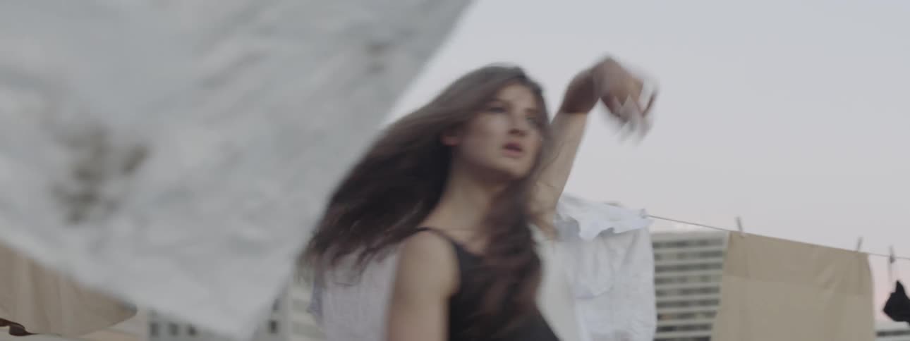 A woman dances on a rooftop amidst clothes lines