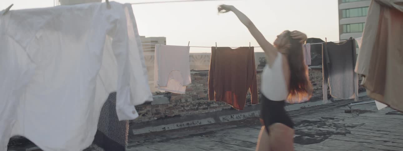 A woman dances in between clothes lines on a rooftop