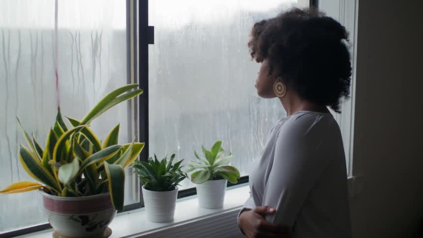 Woman walks to her window to look at the rain outside