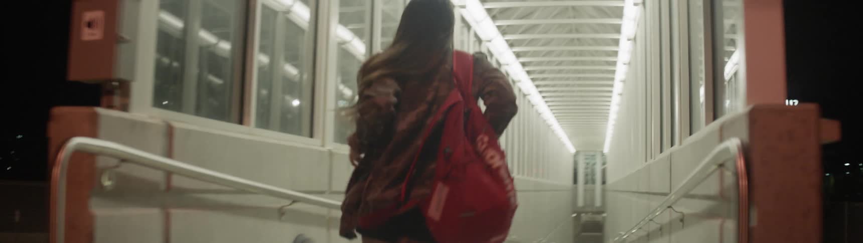A woman with an army fatigue jacket and a red book bag running in a train station
