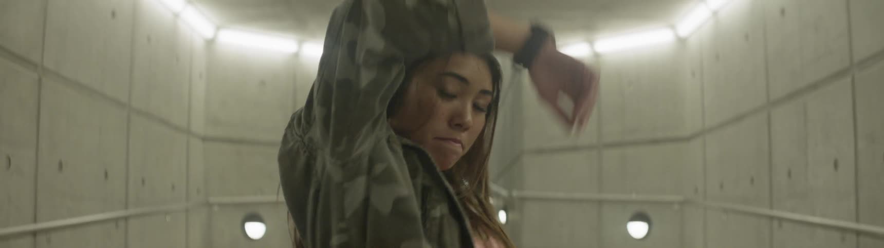 Asian girl wearing headphones and coat dance in underground hall at night
