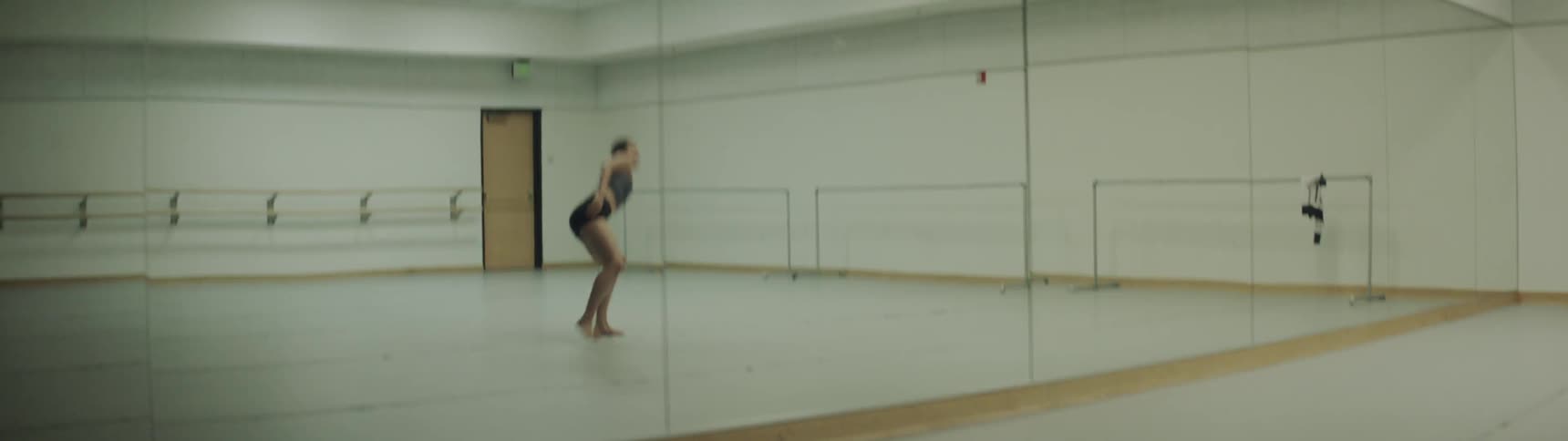 A young and athletic woman dances in a dance studio in front of a large mirror and performs an intense modern dance