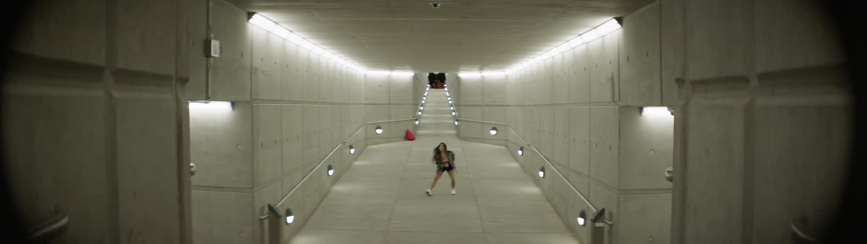 A young woman is performing a modern hip hop dance within an exceptionally long corridor