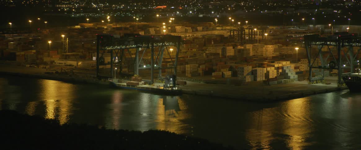 A construction site surrounded by a body of water at night with lights on the numerous buildings