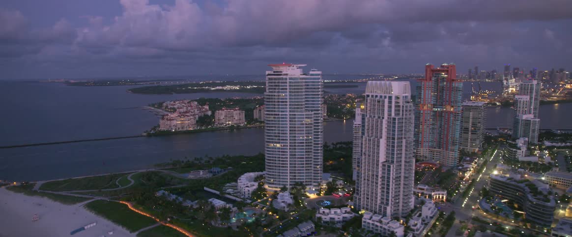 The sky line of a coastal metropolis can be seen illuminated in the early evening and a large cruise ship is passing through its harbor
