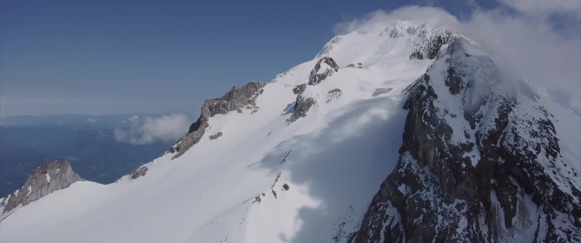 A mountain peak covered in snow surrounded by clouds