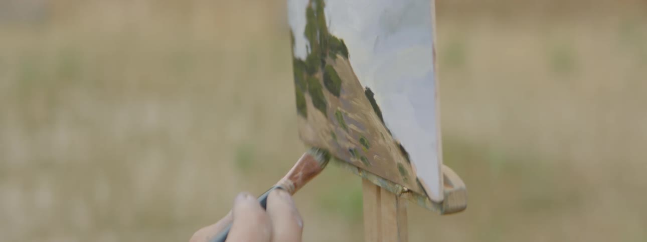 A painter paints a landscape while standing in a field