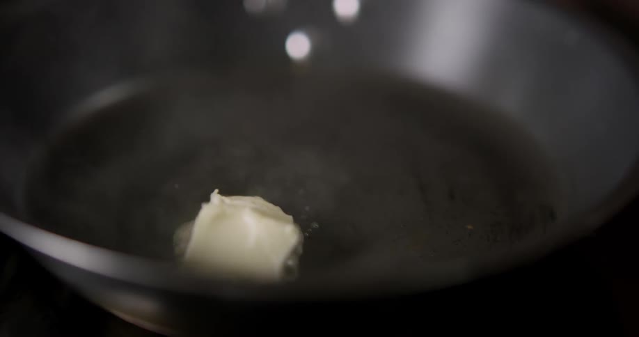 A man melts butter in a pan on a stove in the kitchen.