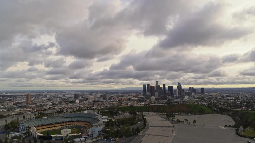 The camera looks over a large city and baseball stadium