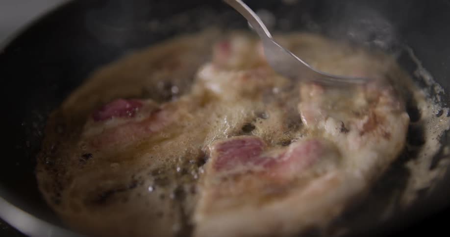 Sizzling bacon flips in a pan in slow motion.