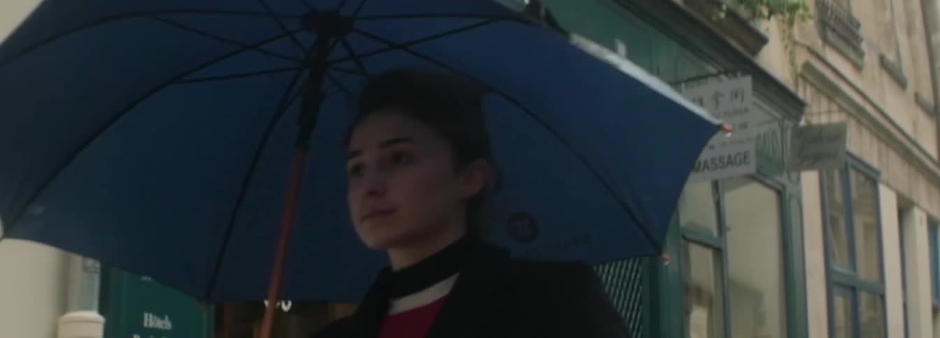 A woman walks down a sidewalk holding an umbrella in the rain