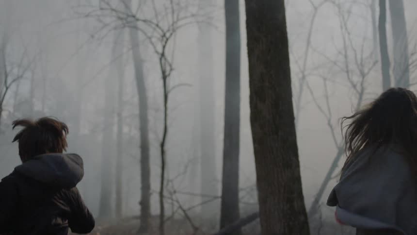A boy and girl run in a foggy forest