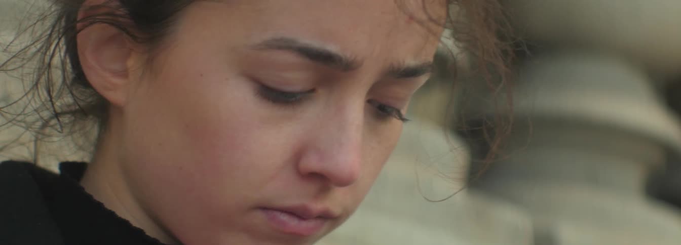 A woman sadly looks down as the wind blows through her hair
