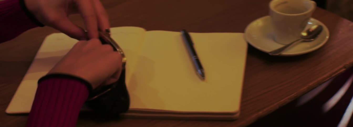 Woman opens her wallet and takes out some coins on the table at dimly lit place