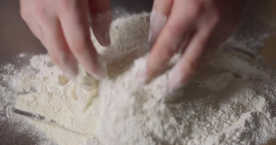 A chef pouring flour onto a table and making a hole in the center of the pile