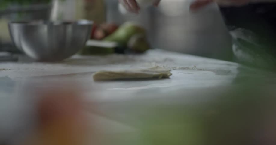 A chef pounds and rolls out dough on a countertop