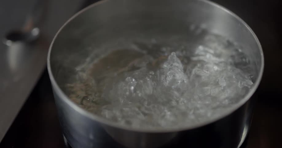 A persons hand is seen lowering the metal lid and placing it atop a boil pot of water