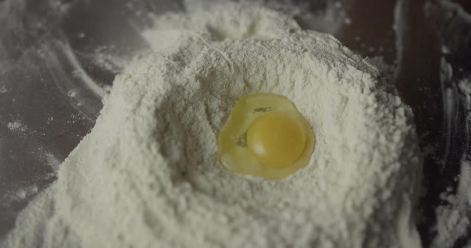 Man breaks egg into the middle of flour