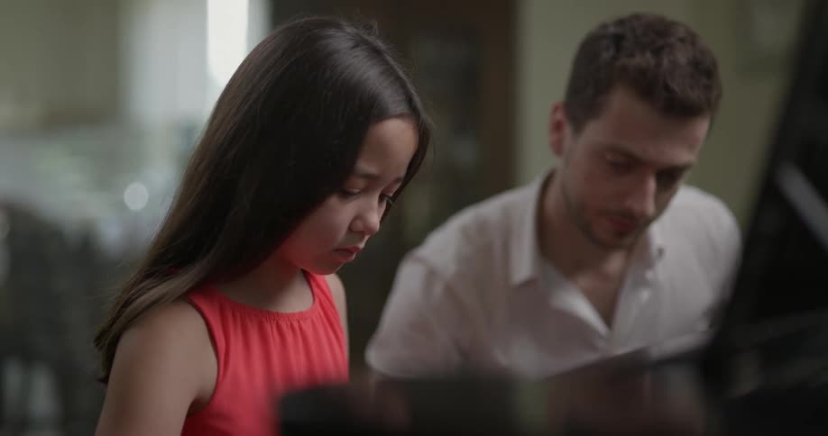 A child plays the piano with an instructor